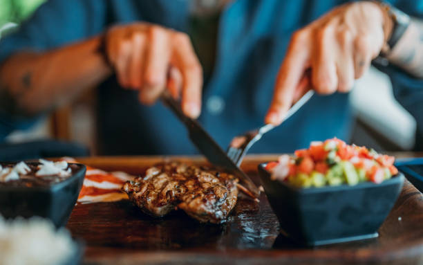 Hands holding fork and knife and eating delicious juicy steak on a wooden plate